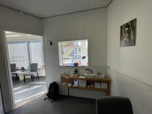 Kantoorruimte aan de Prinses Mariannelaan met een zithoek, wandplank met apparaten en een raam met uitzicht op de straat.